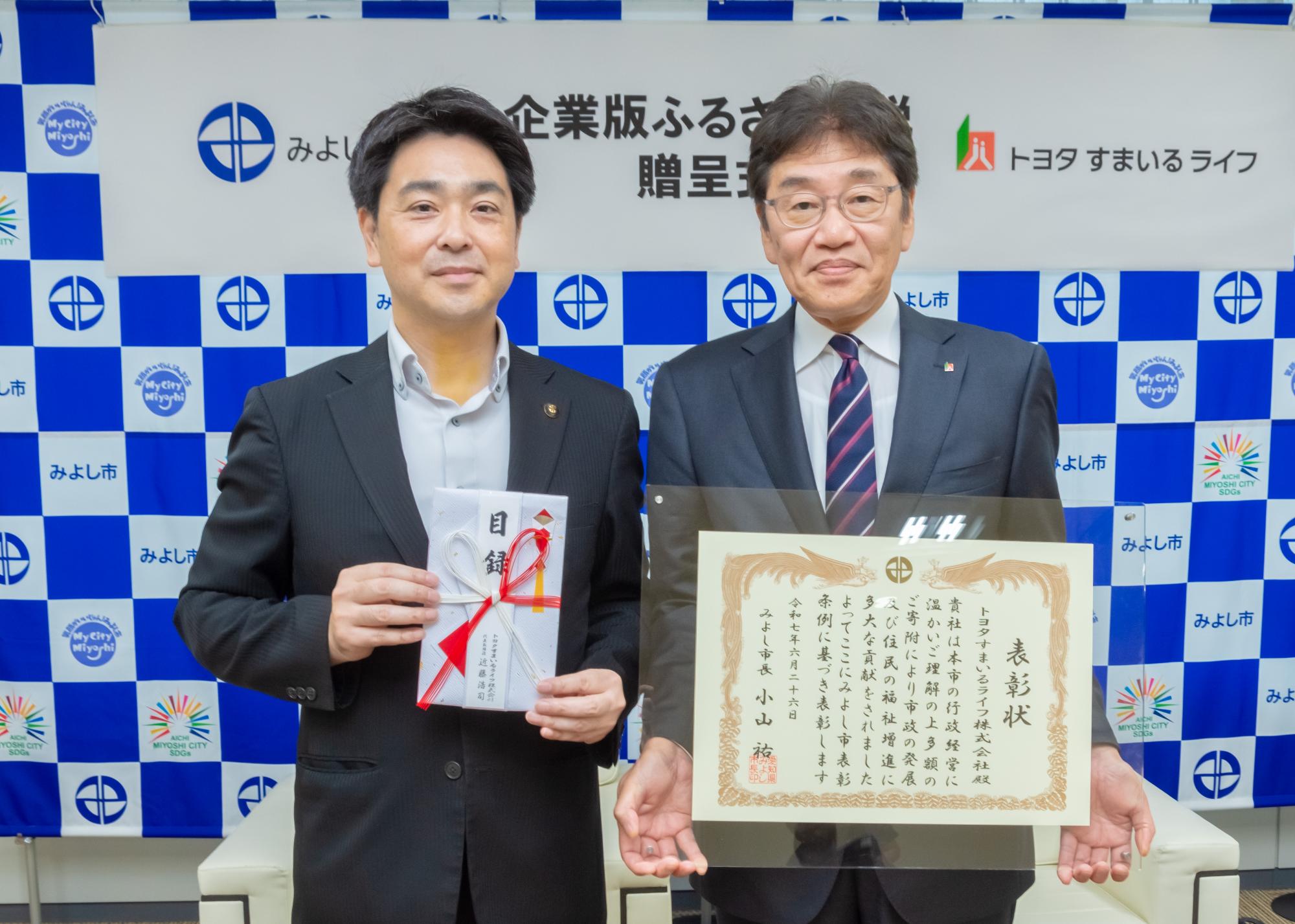 みよし市のバックボードの前で市長と近藤代表取締役が表彰状を持ち記念撮影をしている写真
