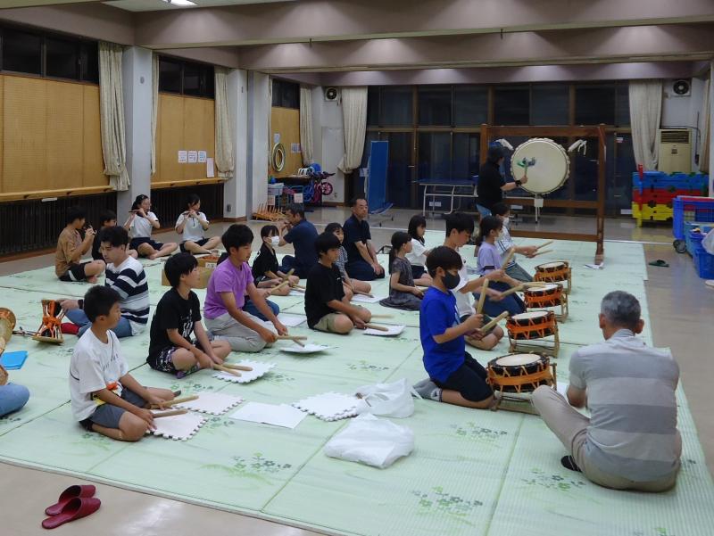 締太鼓の練習をしている子供たちとそばで指導をしている男性の写真