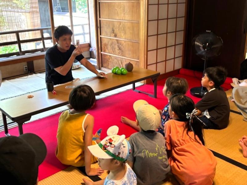 長机でマジックを披露している男性とマジックを見ている子どもたちの写真
