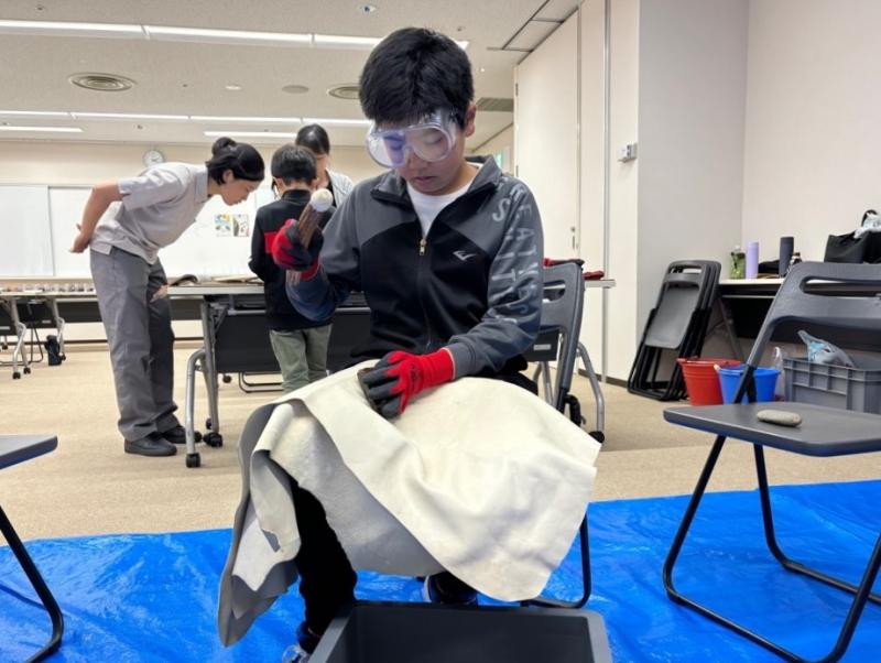 鹿の角を黒曜石に打ち付けようと振りかぶっている男の子の写真