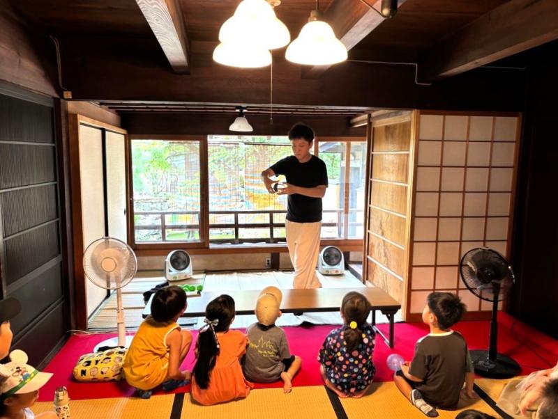 立ち上がってマジックを披露している男性とマジックを見ている子どもたちの写真
