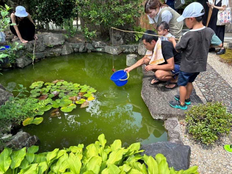 池のふちに立って釣竿を垂らしてザリガニ釣りをしている男の子の写真