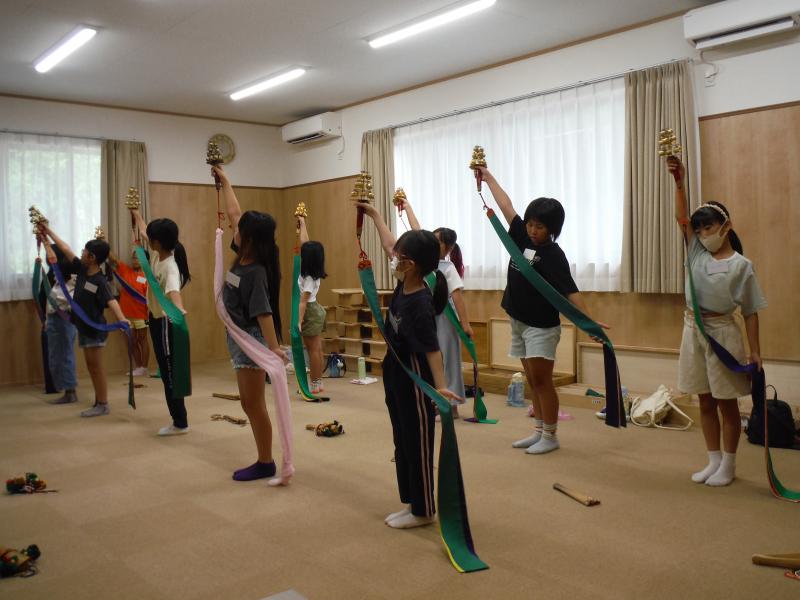 長いストールのような布がついた巫女鈴をもって踊りの練習をしている子どもたちの写真