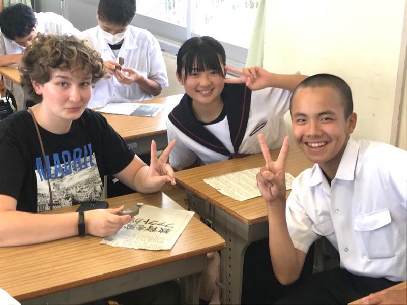 席に座っているコロンバス市から来た生徒と三好中学校の女子生徒と男子生徒がカメラに向かって笑顔でピースサインをしている写真