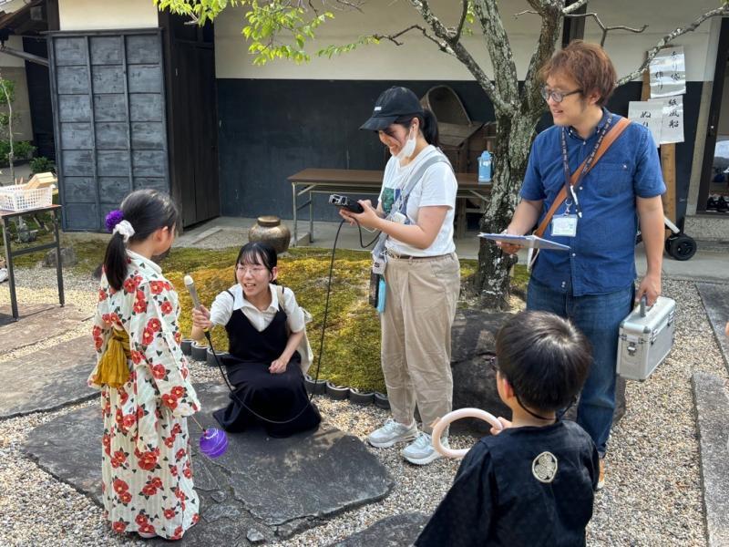 赤い花柄の浴衣を着た女の子がテレビクルーにインタビューを受けている写真