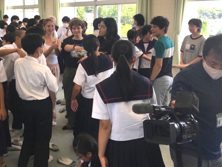 テレビカメラが来ている教室内でコロンバス市から来た高校生と中学生たちが楽しそうに交流をしている様子の写真