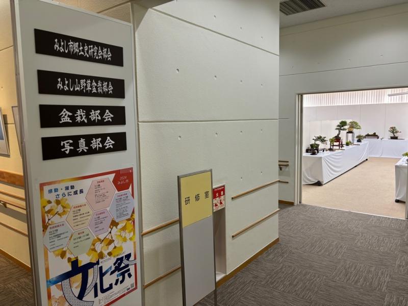 左側に展示の案内とポスターが掲示されており、入り口の奥に盆栽が並んでいる写真