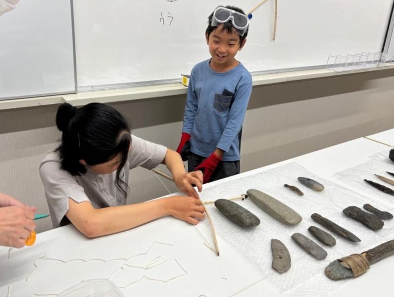 木の棒に矢じりをつける作業をしている親子の写真