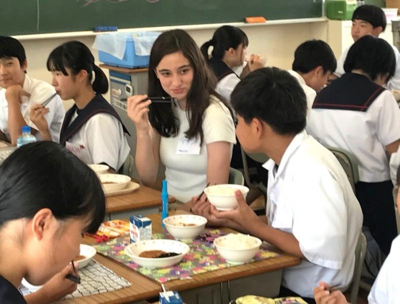 グループに分かれ机を合わせて座っているコロンバス市から来た女子高校生と中学生たちが一緒に給食を食べている写真