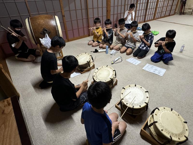 正座で締太鼓をたたいている子供たちと横笛を吹いている子どもたちの写真