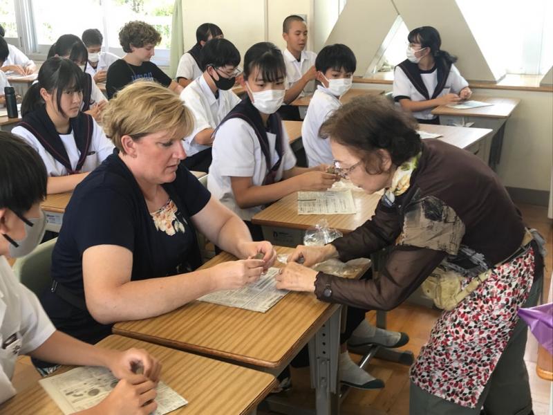 年配の女性が、三好中学校の生徒たちの間の席に座っているコロンバス市から来た女性に箸置きづくりのアドバイスをしている様子の写真