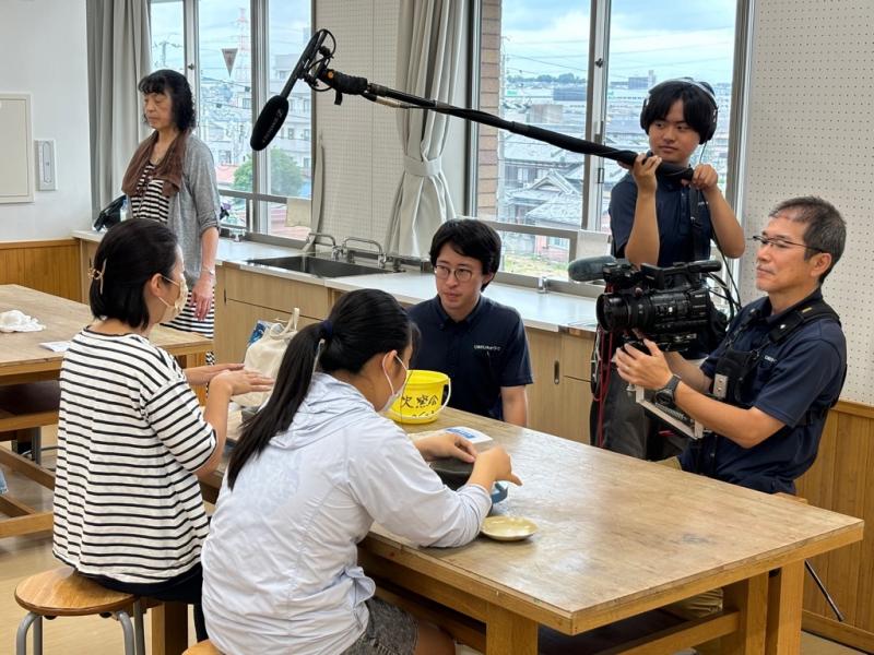 焼き物を作っている二人の女性にマイクやカメラを向けて撮影しているテレビクルーの写真