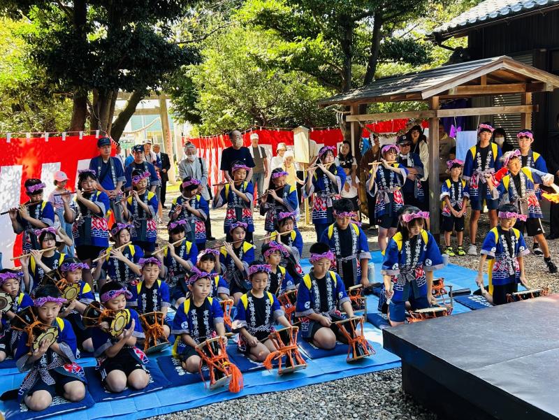鉢巻を巻いて法被を着ている子供たちが、一列目は小鼓、2列目、3列目は横笛を演奏している写真