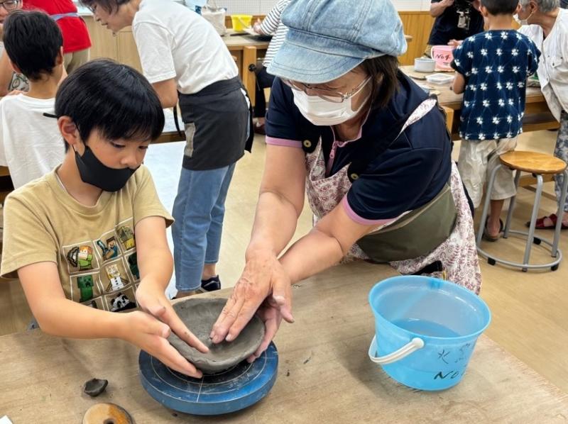 ろくろの上でお皿のふちを整えている男の子と横で手伝っている女性の写真