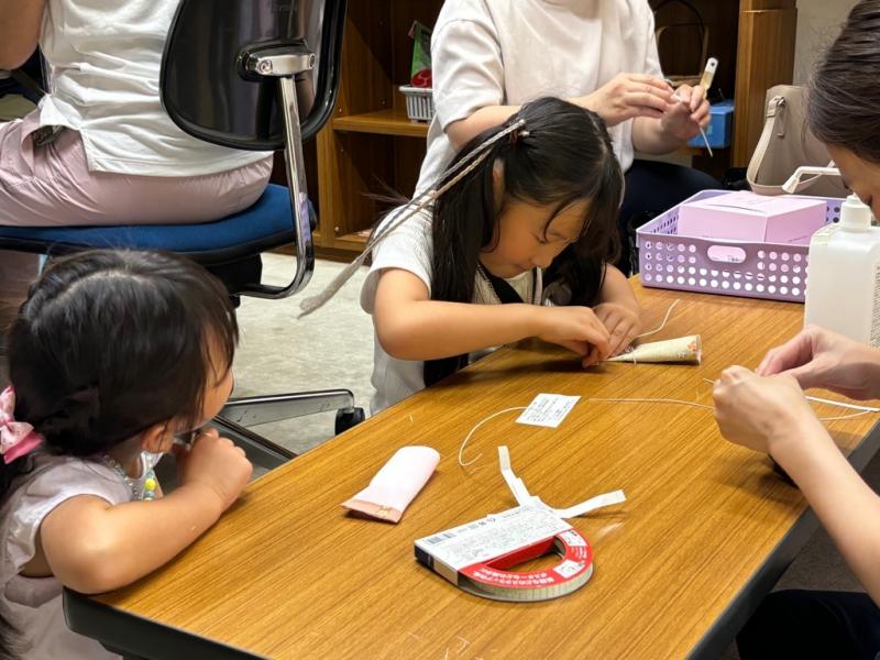 紙を折って工作をしている女の子と、隣で見ている女の子の写真