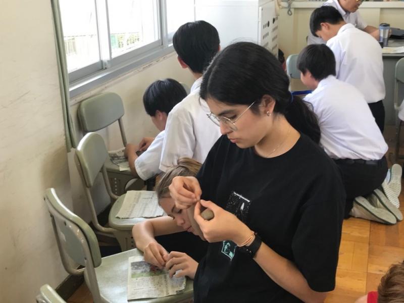 黒髪を1つにまとめて結んでいるコロンバス市から来た生徒が真剣に粘土を形成している様子の写真
