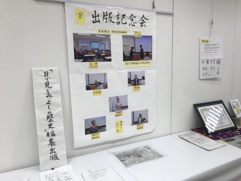 「目で見るみよしの歴史」編集出版と書かれた横の壁に「8 出版記念会」と書かれて7枚の写真が貼られて新聞なども展示されている写真