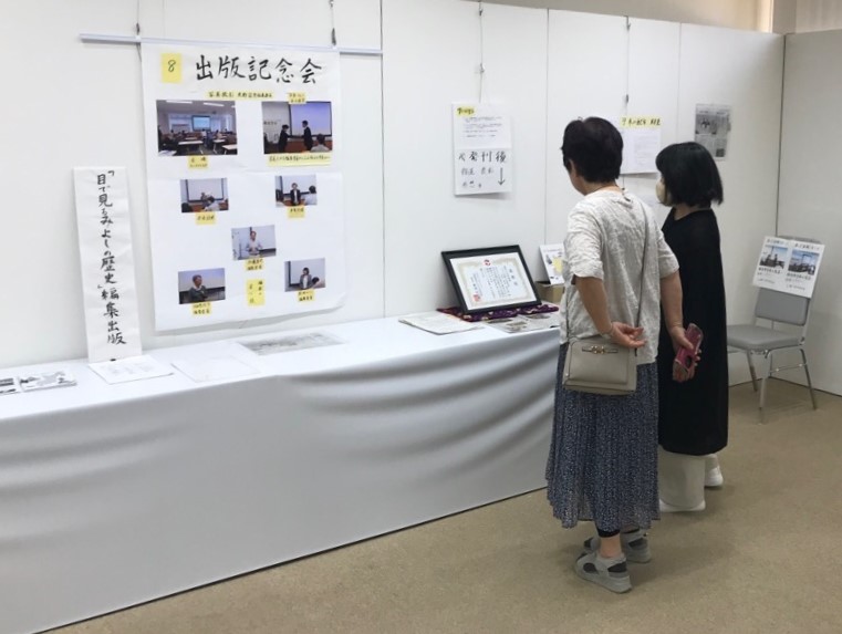 「目で見るみよしの歴史」編集出版と書かれた横の壁の展示物を女性2名がじっとみている様子を写した写真