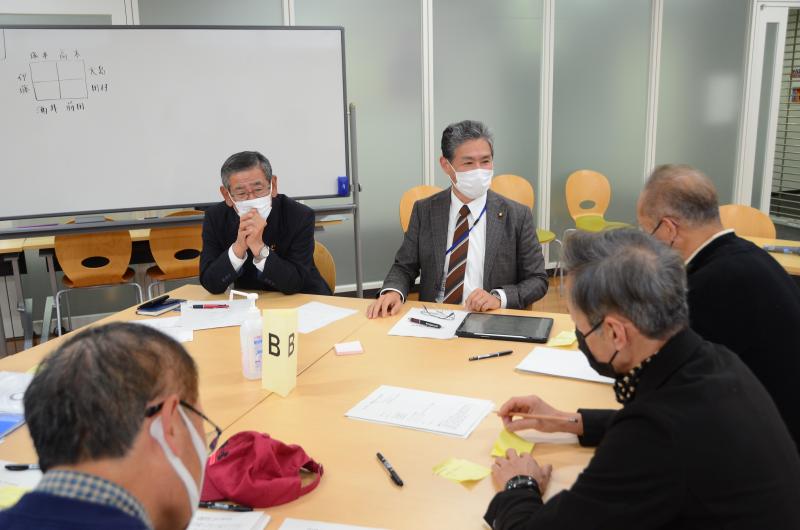 向かい合わせで設置された長机に参加者達が座り、話し合いが行われている様子の写真