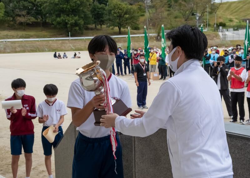 右側に選手が整列し、下に賞状を受け取った2人が立っており、市長が学生に優勝カップを渡している写真