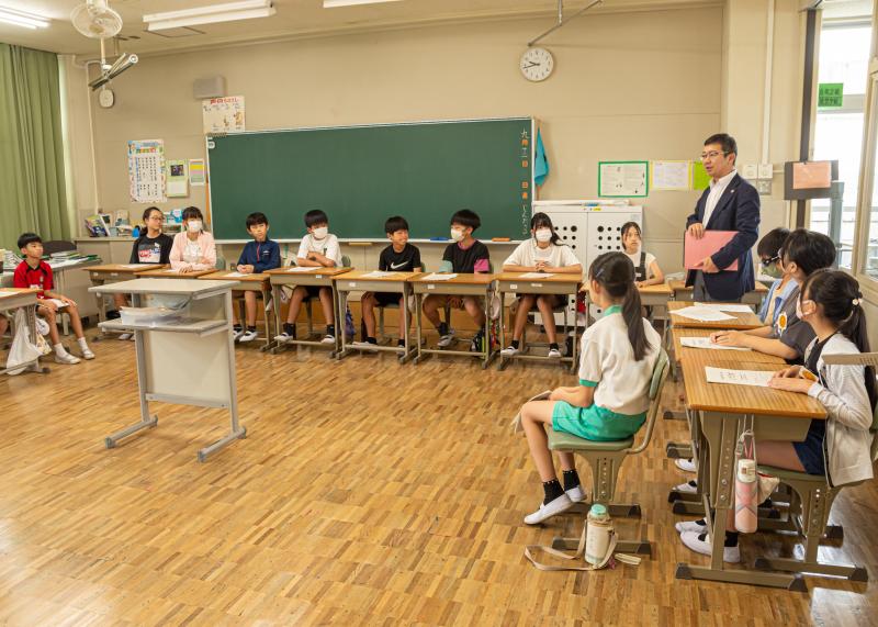 机を法廷のように並べた教室で、愛知県弁護士会西三河支部の松山さんが模擬裁判前に挨拶をしている写真
