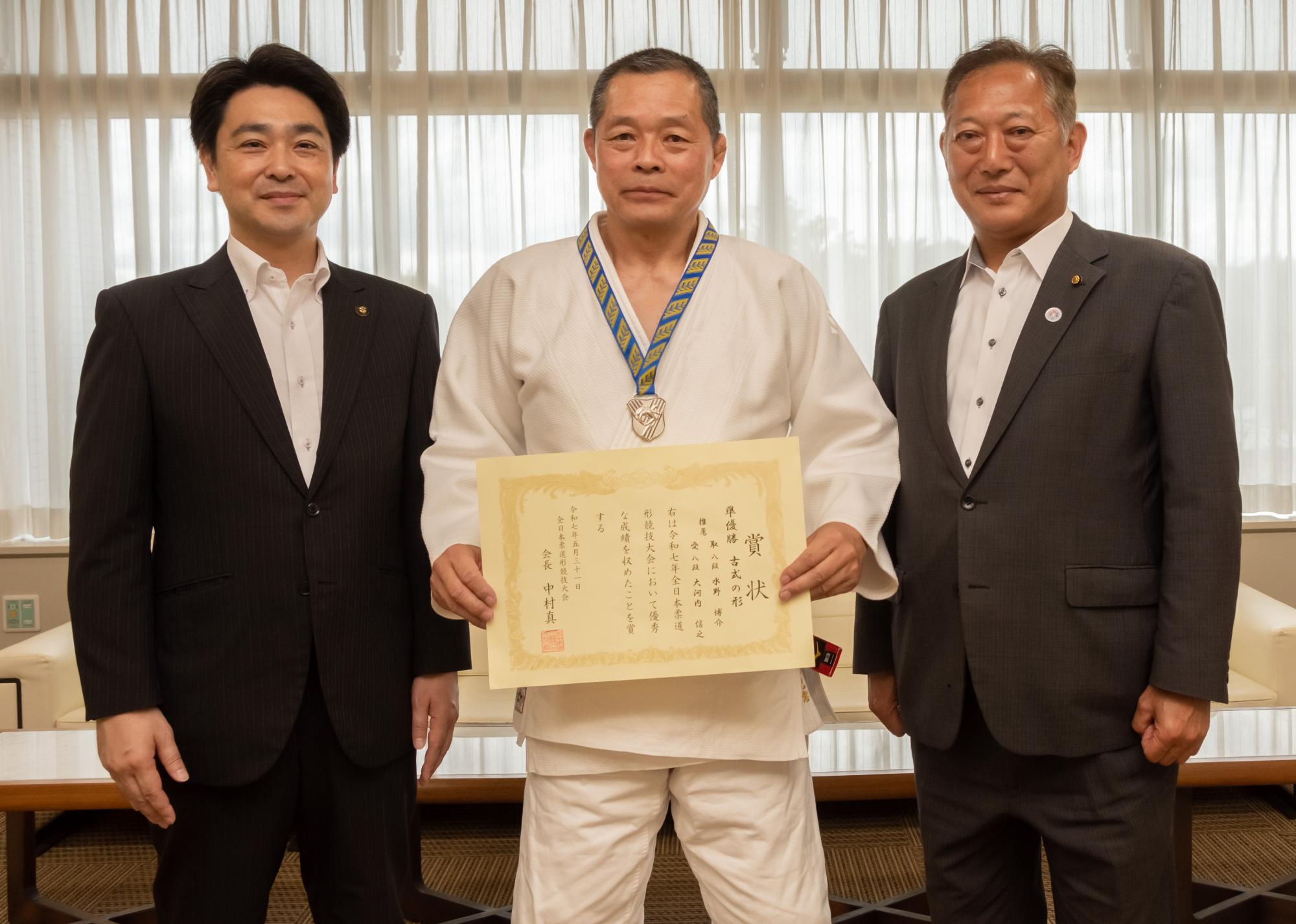 メダルを首にかけ、賞状を持つ水野さんを挟んで、市長と教育長と3人での写真