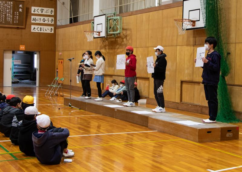 三好丘小学校の児童の1人がクイズを出題し、3人が回答の選択肢を持って立っている写真