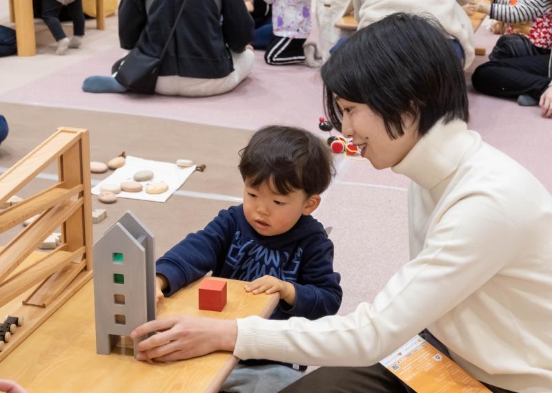 細長い家のような形の木のおもちゃで遊ぶ男の子と母親の写真
