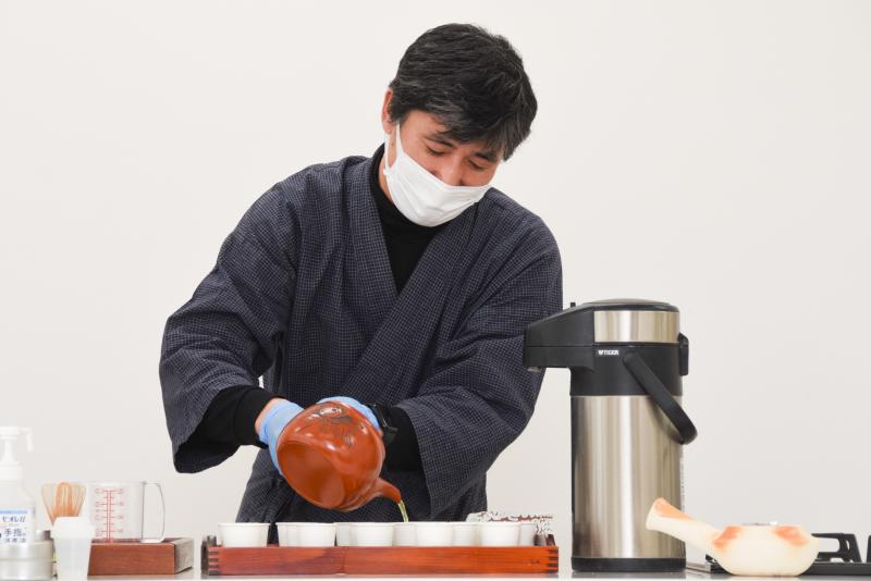 野場義尊さんが並べられた紙コップに急須でお茶を注いでいる写真