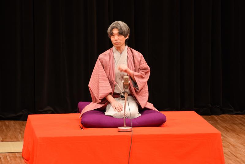 赤い高座台の上に座っている微笑亭さん太さんを正面から写した写真
