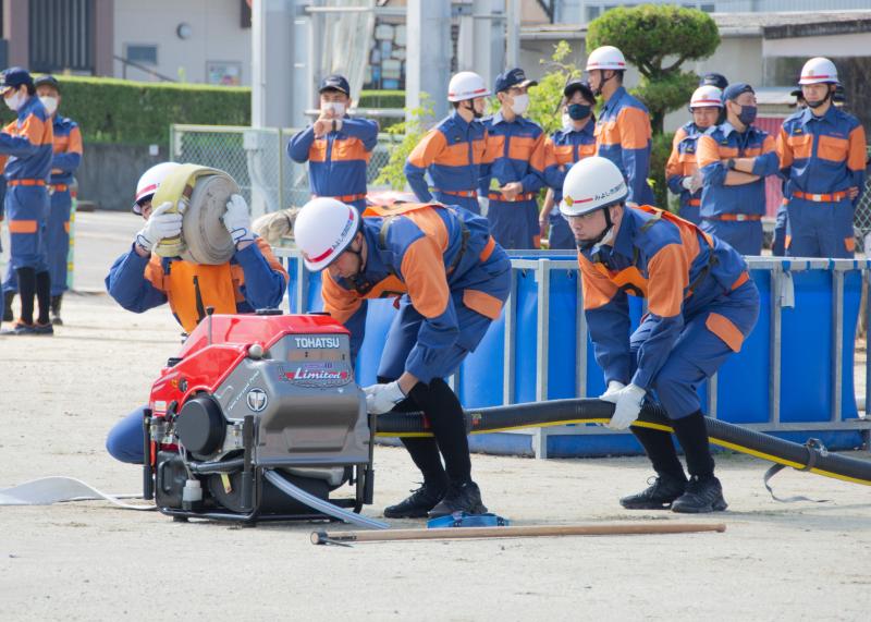 小型ポンプを2名の団員で準備をし、結合するホースを肩に抱えた団員が跪いて待機している写真