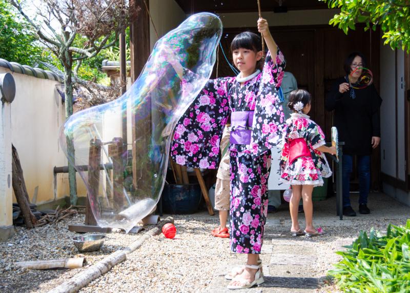浴衣を着た女の子が巨大なシャボン玉を作って遊んでいる写真