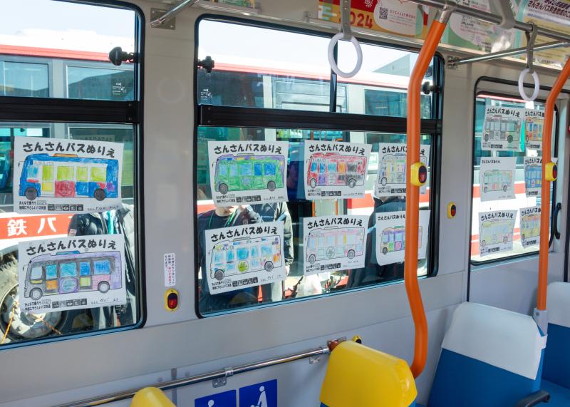 「さんさんバスぬりえ」と書かれた紙に色塗りされたバスのイラストが、バスの窓に沢山貼られている写真