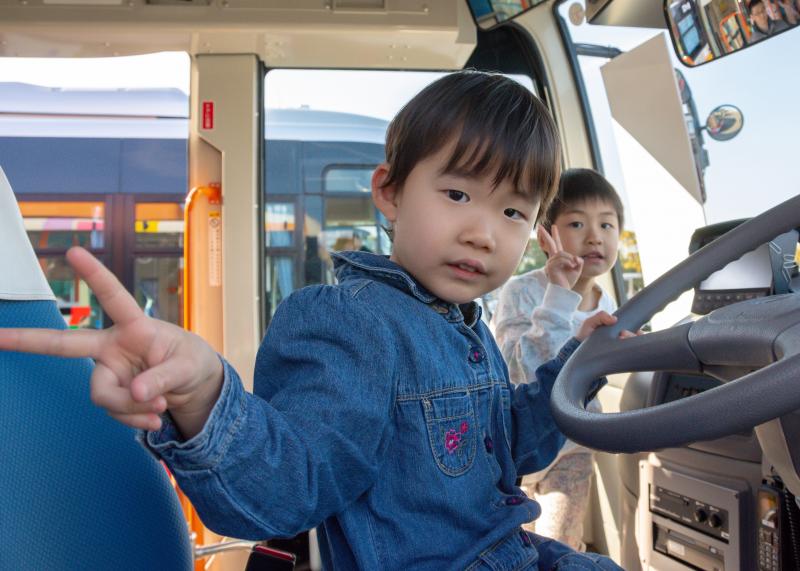 バス乗車体験で運転手席に座りピースサインをしている男の子の写真