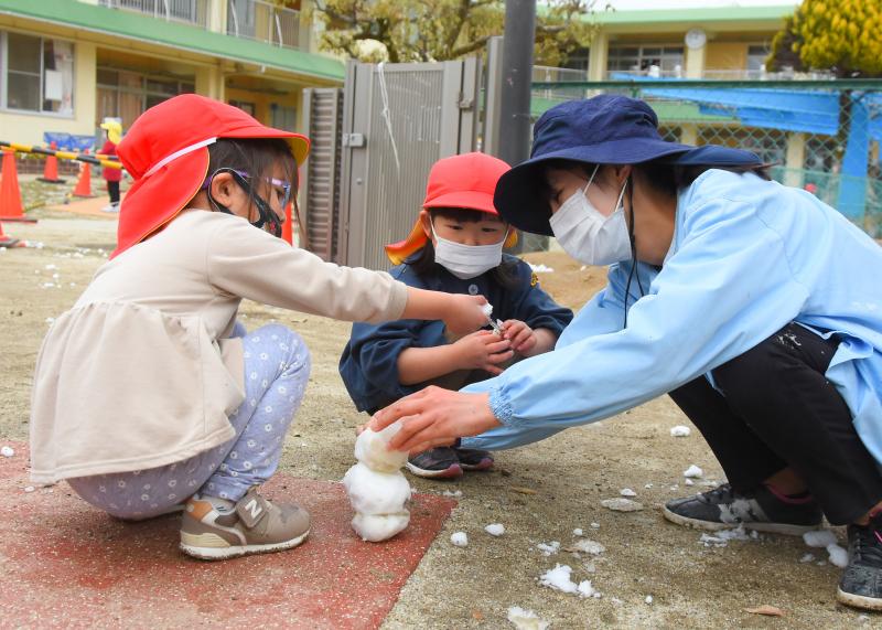 女の子と男の子が先生と雪だるまを作っている様子の写真
