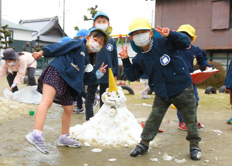 男の子2人と女の子が園児の腰ぐらいまである雪だるまと記念撮影している写真