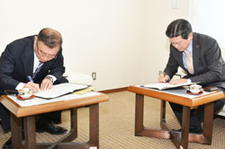 協定書にサインする小野田市長と宮﨑専務役員