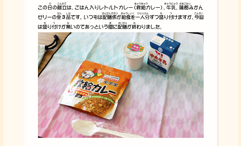 布の上に救給カレー、みかんゼリー、牛乳が置かれている写真