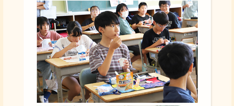 ボーダーのTシャツを着た男子児童がスプーンでみかんゼリーを食べている写真