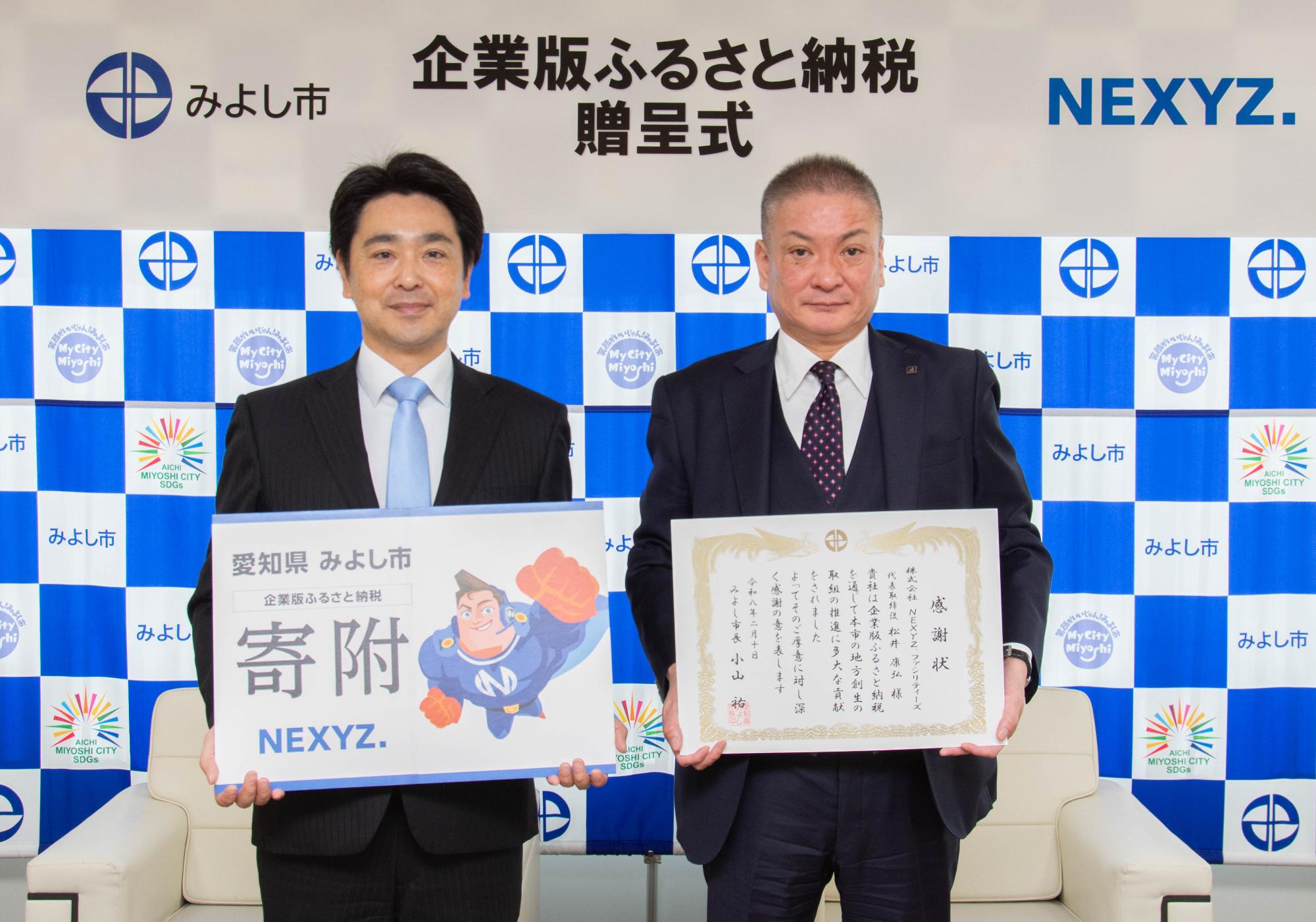 みよし市のバックボードの前で市長と大前取締役副社長が感謝状を持ち記念撮影をしている写真