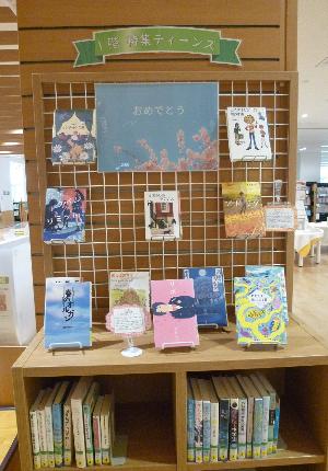 1階ティーンズと書かれ本棚の上や吊るし棚に本が飾られ紹介されている写真