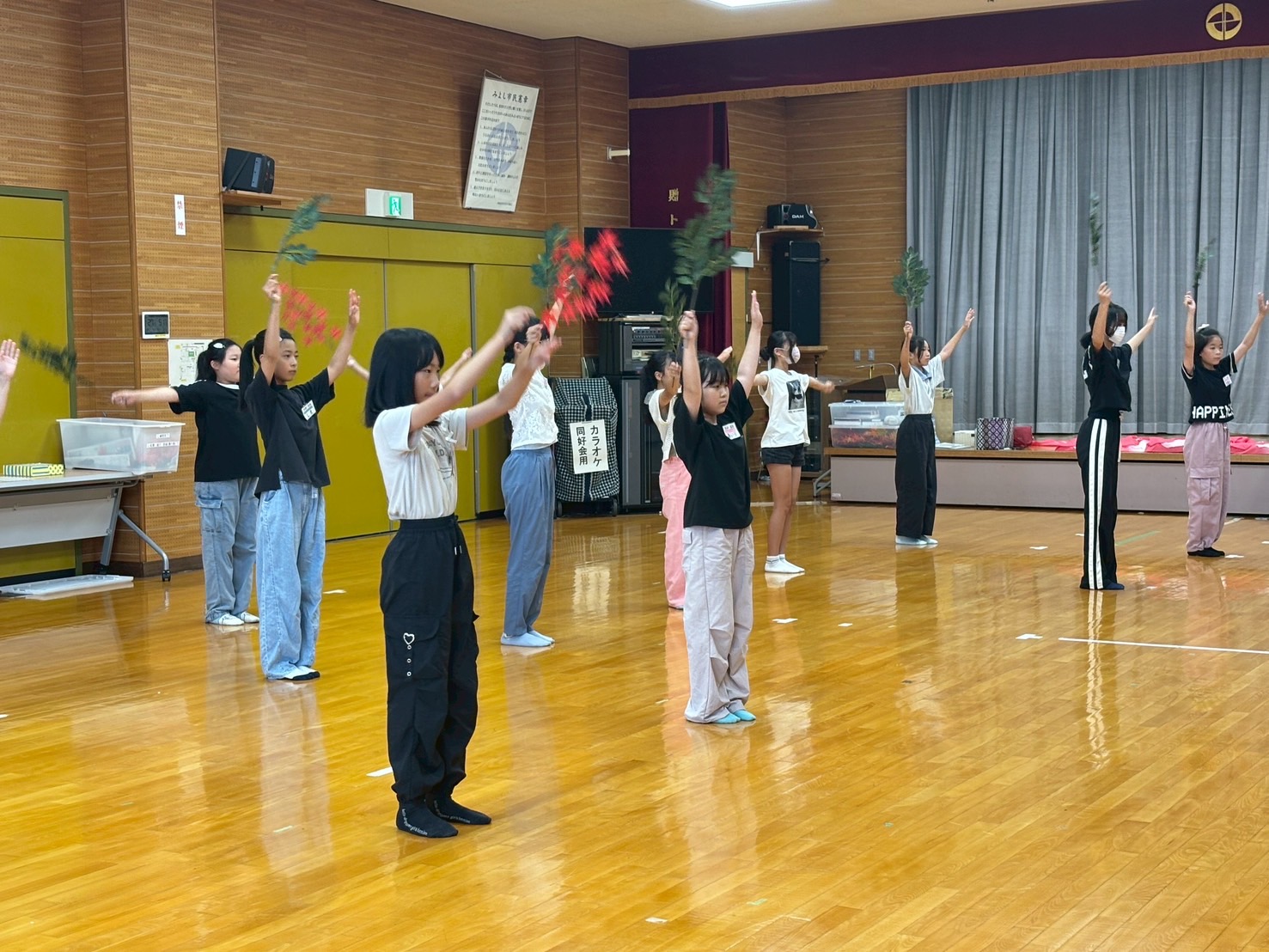 体育館で右手に道具を持ち両手を上げる子どもたちの写真