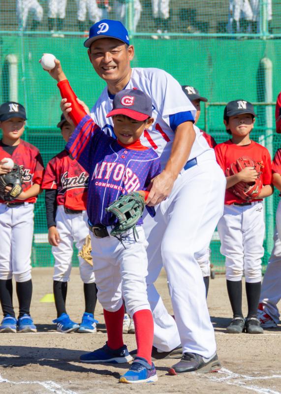 軟式野球体験教室でピッチングの仕方を教わる男の子とフォームをレクチャーしている川上憲伸さんの写真