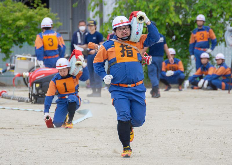 綺麗に巻かれた消化ホースを左肩に乗せ、左手で支えながら走る消防団員の写真