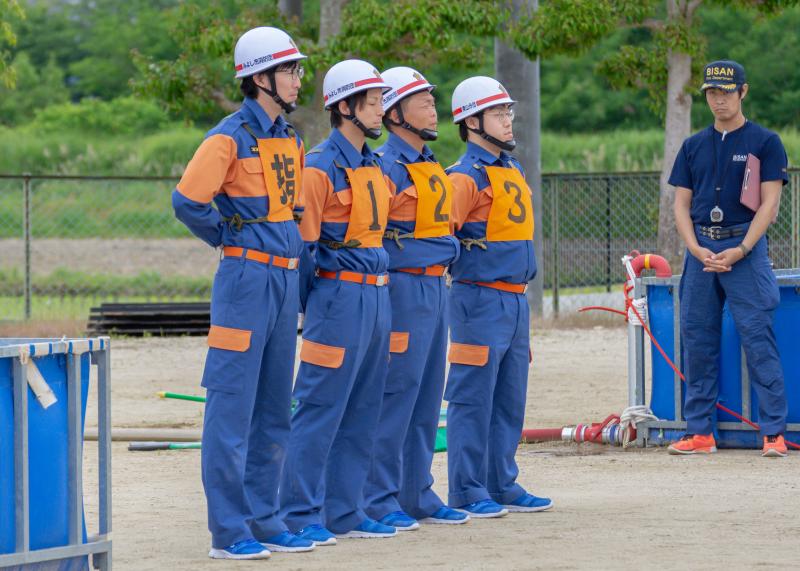両手を後ろに組み足を広げて立つ4名の消防団員の写真