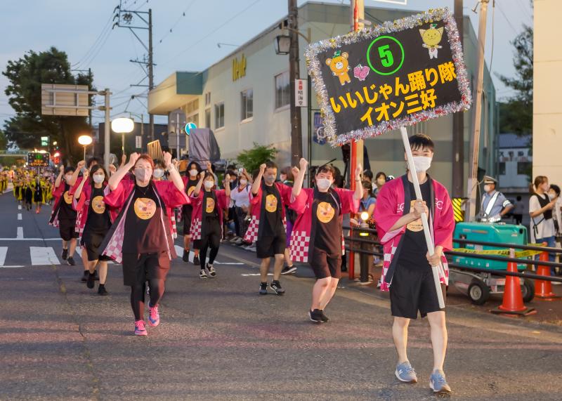 いいじゃん踊り隊イオン三好のプラカードを持った人の後ろをピンク色の法被姿の方々が踊っている写真